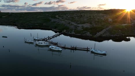 las llamaradas del sol brillan por encima de la cresta en el muelle natural del puerto de sa nitja menorca, españa, el agua tranquila refleja el cielo nublado