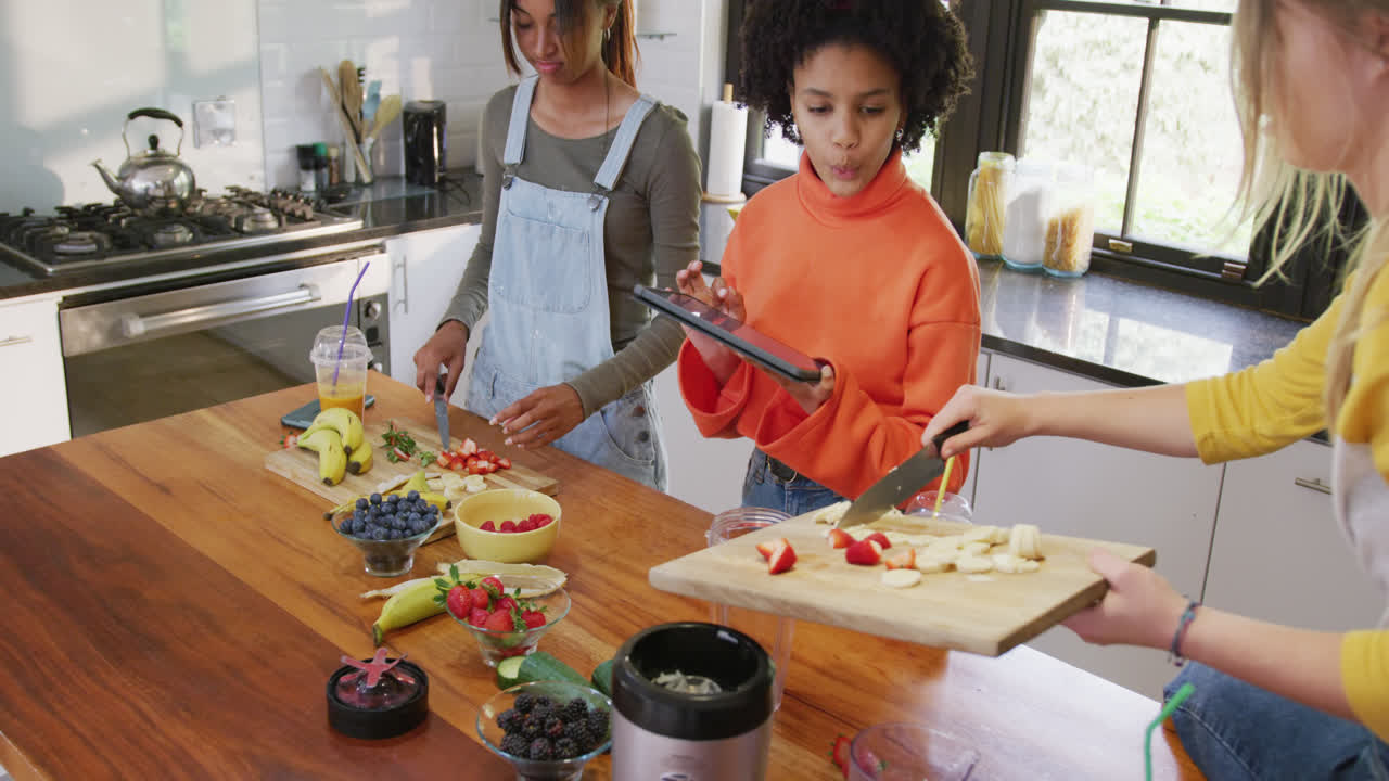 diversas amigas adolescentes cortando frutas usando tableta en la cocina, cámara lenta