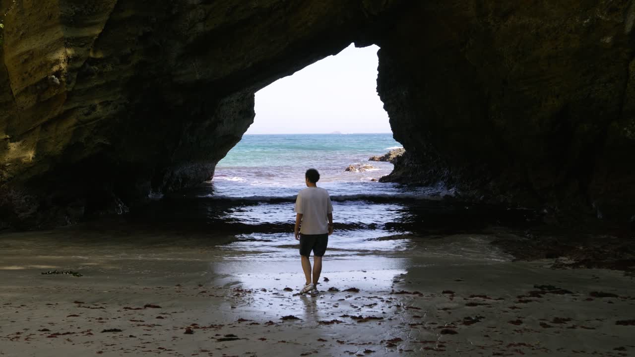 Barefoot male walking towards deep ocean inside dark sea cave