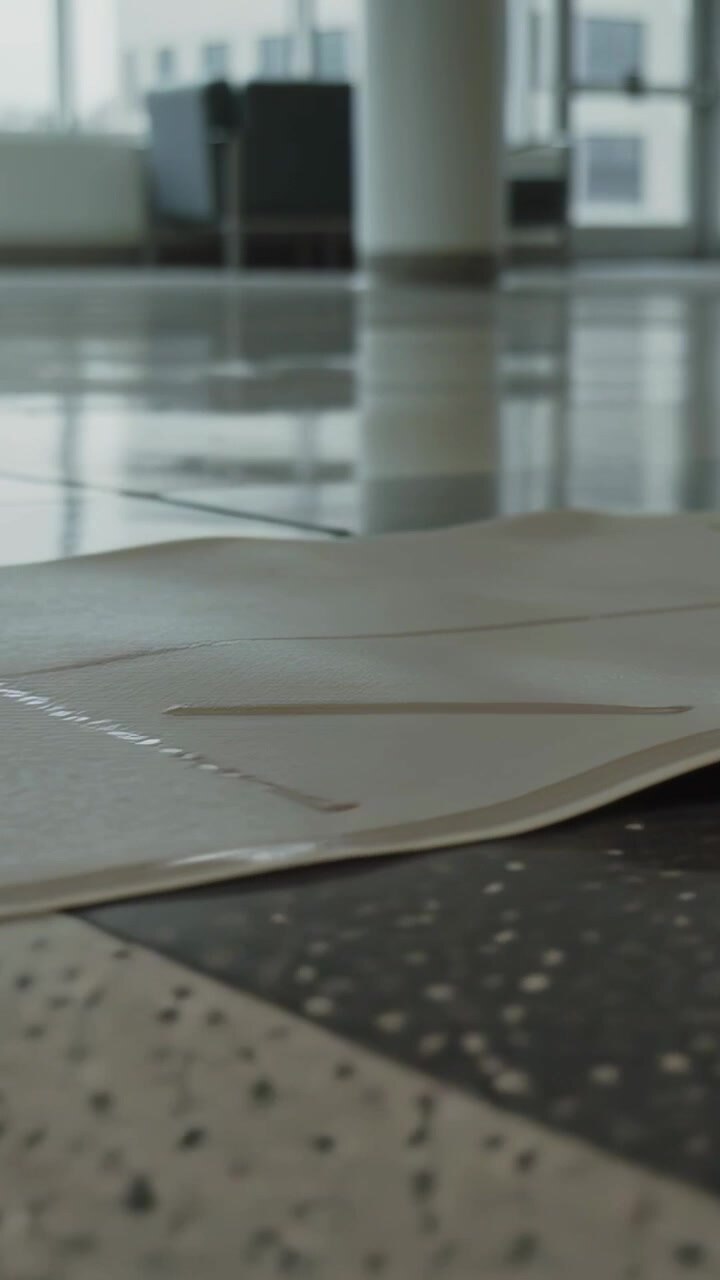 Vertical video: Tilting camera revealing cardboard sheet flattening on atrium floor, taped seams