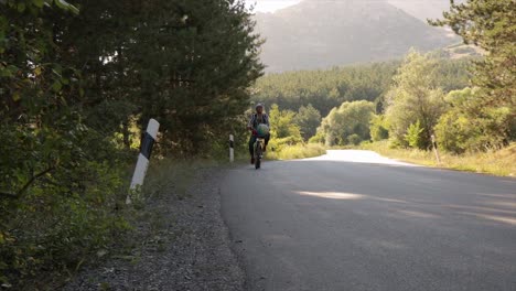 Man-riding-a-bicycle-on-an-open-road-through-forest