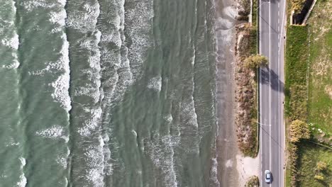 top down aerial footage of long waves on a beach next to the road