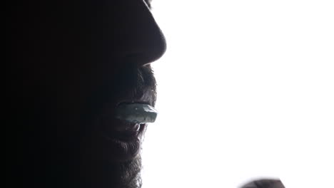 Backlit-bearded-male-putting-dental-oral-alignment-retainer-on-teeth-for-protection-against-grinding