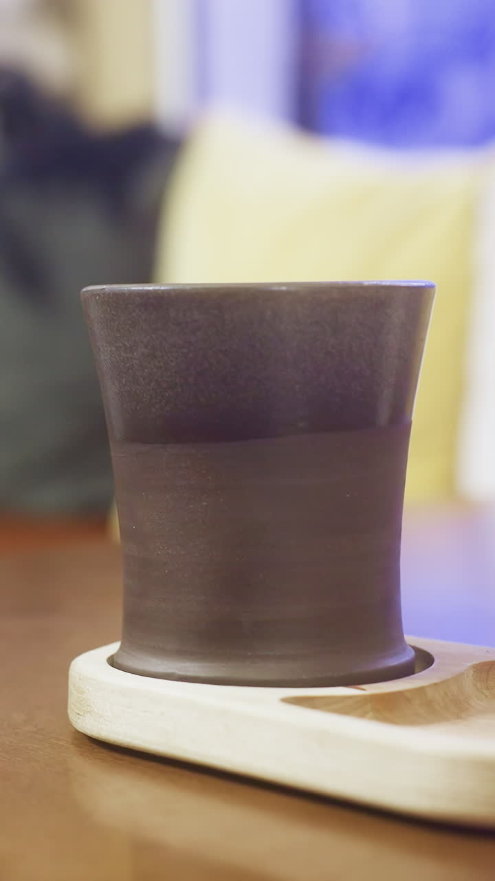 Side shot of lady's hand in brown shearling jacket gently lifting cup of coffee at cozy cafe table, with soft lighting enhancing the warm and inviting atmosphere perfect for relaxation