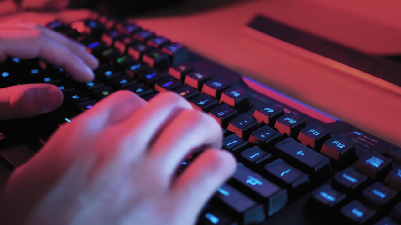 un primer plano de las manos escribiendo en el teclado con luz apagada roja - azul