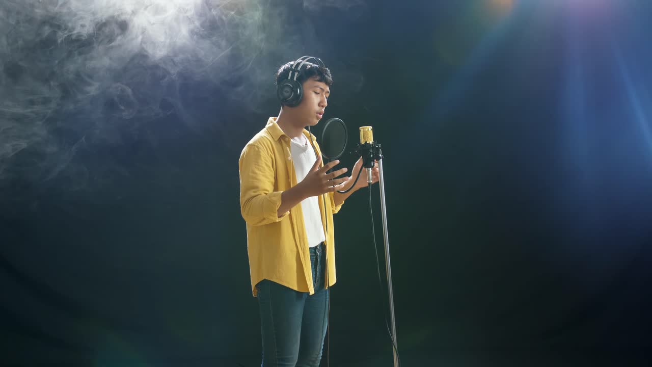 joven asiático con auriculares cantando en un micrófono condensador en el fondo blanco de humo negro