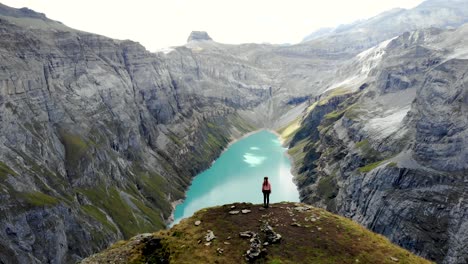 a standing hiker enjoying the view over lake limmernsee in glarus, switzerland, the turquoise colored water of which is surrounded by tall swiss alps peaks and cliffs