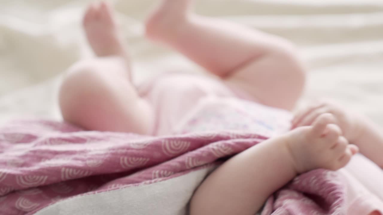 niña recién nacida sana con ropa rosa, moviéndose en la cama