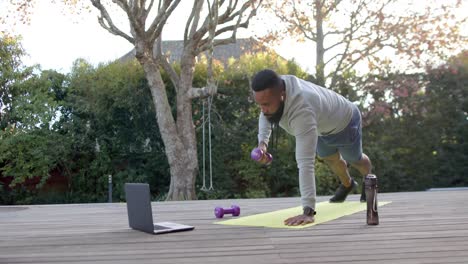 African-american-man-fitness-training-exercising-with-weights-on-deck-in-sunny-garden,-slow-motion