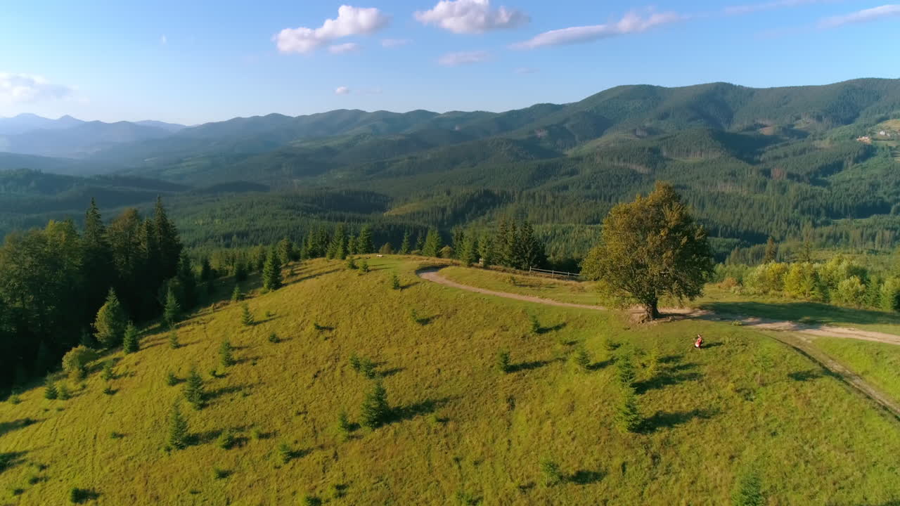 Amazing mountainous area in a sunny day. Flight over the green hill. Musician performing music on mountains background. Aerial view.