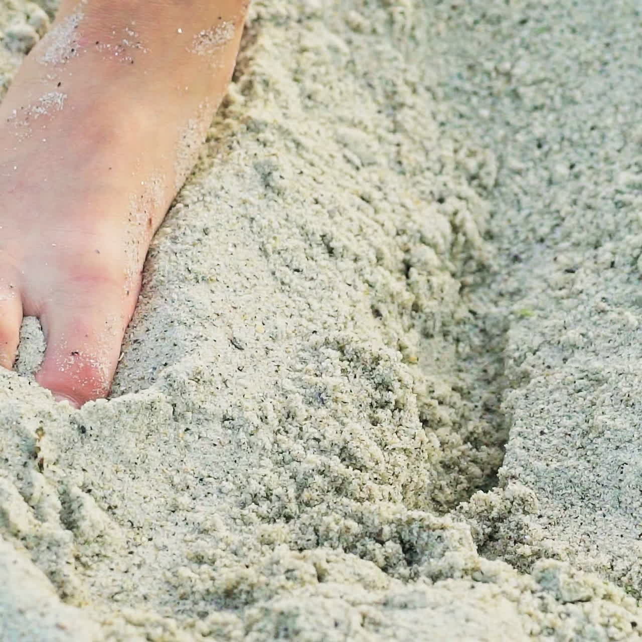 A child digs a pit with his hands in the sand near the sea on vacation. Entertainment at the beach.