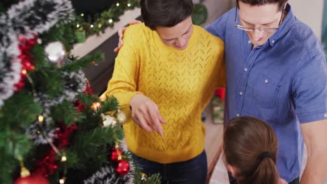 padres caucásicos felices y hija decorando el árbol de navidad en navidad