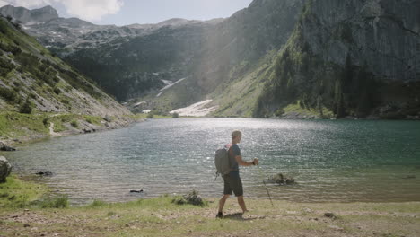 side tracking of a hiker walking with hiking poles near a mountain lake, water in the lake is glistening, mountains in the back