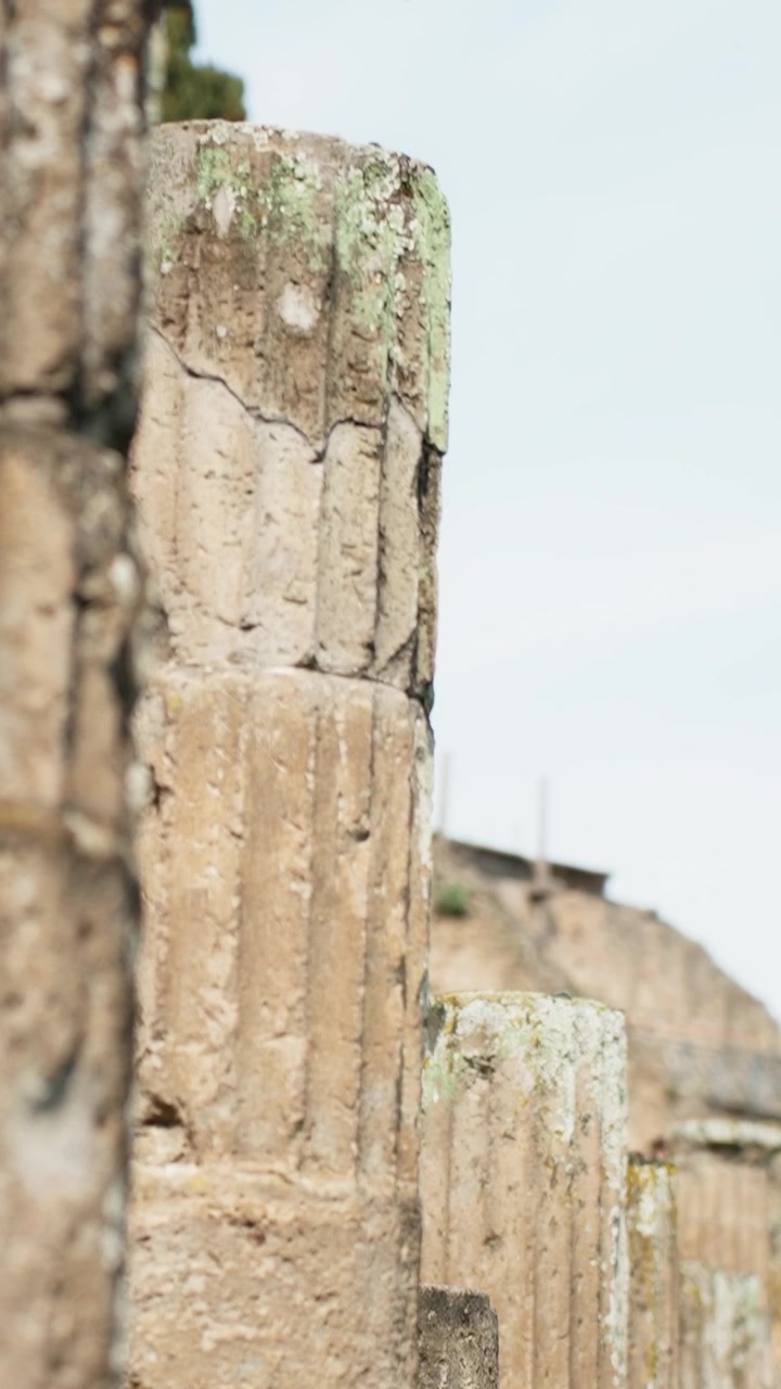 Vista de seguimiento en primer plano a lo largo de antiguas columnas de piedra y mampostería desgastada de Pompeya, mostrando enfoque superficial, texturas rugosas y detalles arqueológicos a plena luz del día.