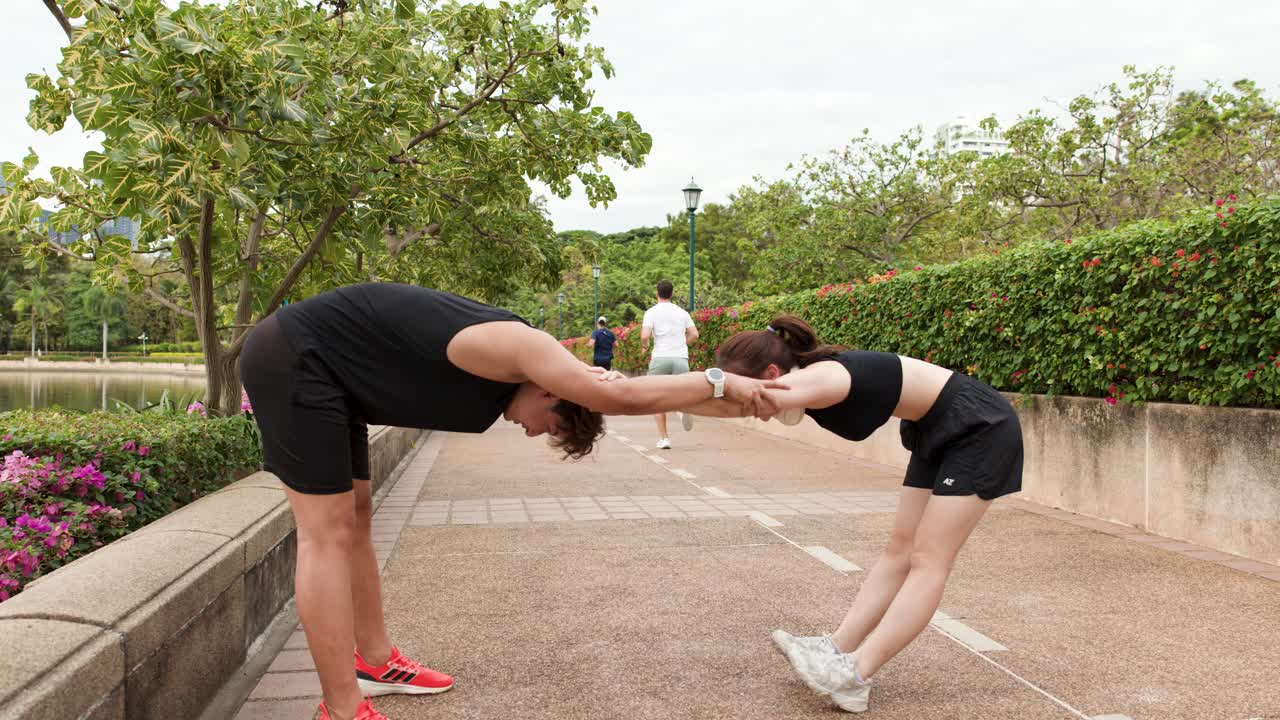 Una pareja tailandesa atlética realiza estiramientos en pareja en un sendero del parque durante un entrenamiento a plena luz del día