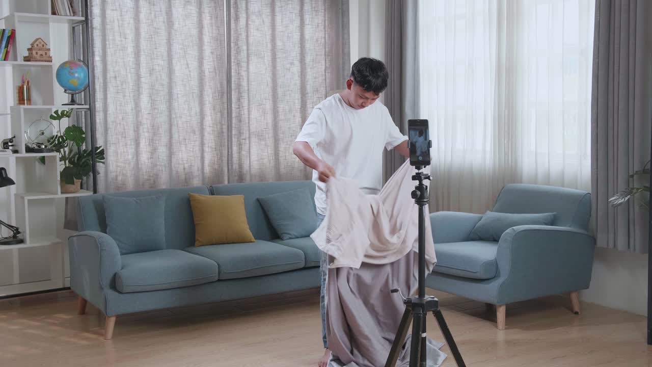 Asian Boy Shows Trick With Disappearing On Mobile Phone Camera While Recording On Smartphone Video Content For Social Networks In Cozy Room