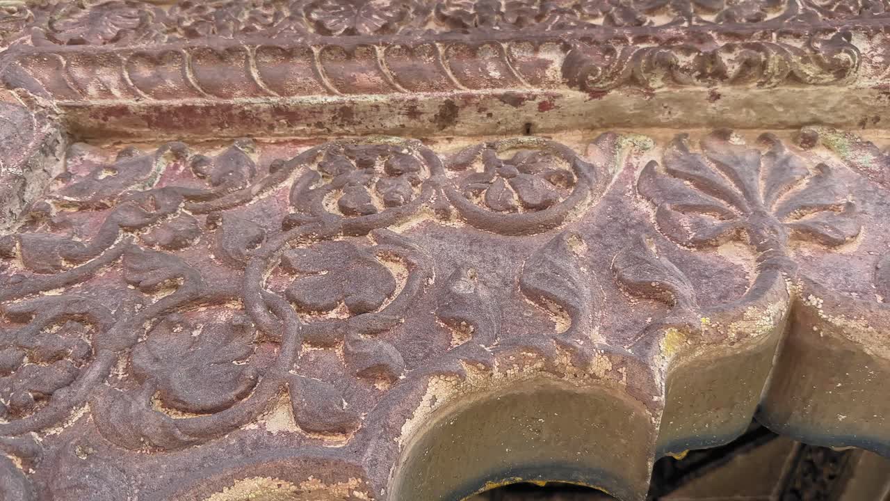 Intricate floral and geometric carvings adorn the aged door surface, showcasing delicate curves and textured patterns highlighted by weathered stone tones and soft natural light