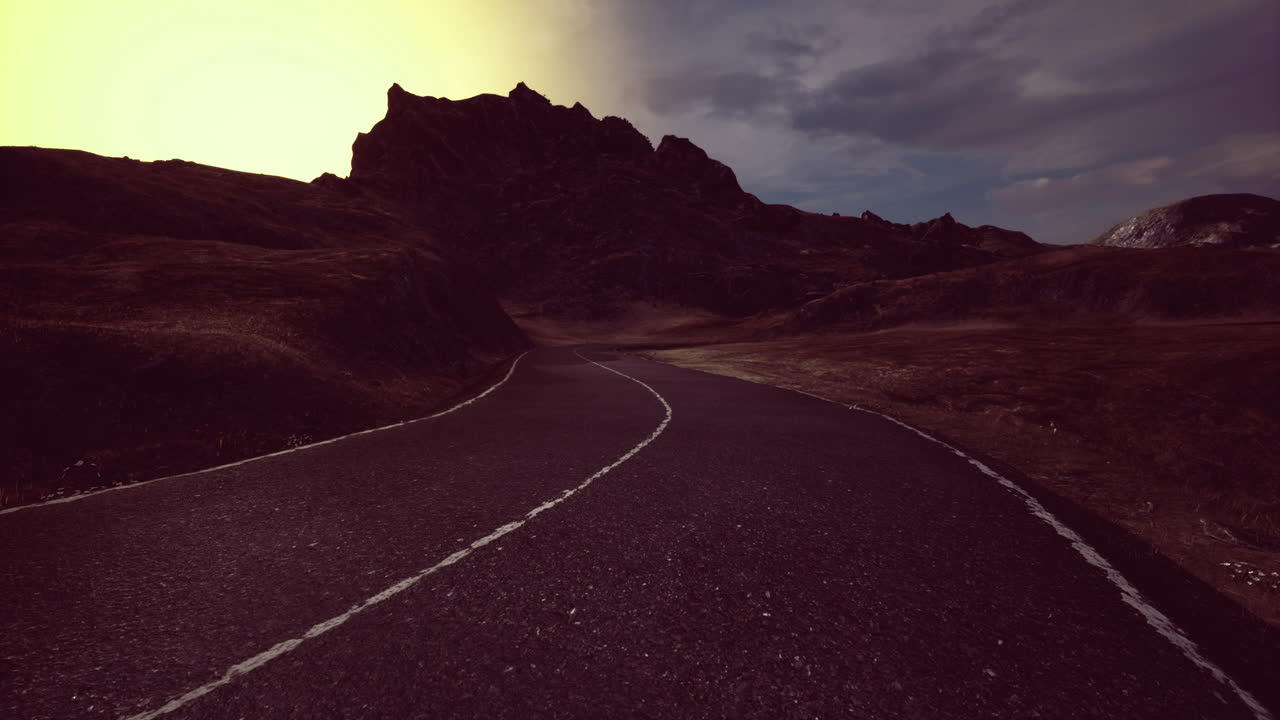 Winding road through rugged mountains under a dramatic sunset sky