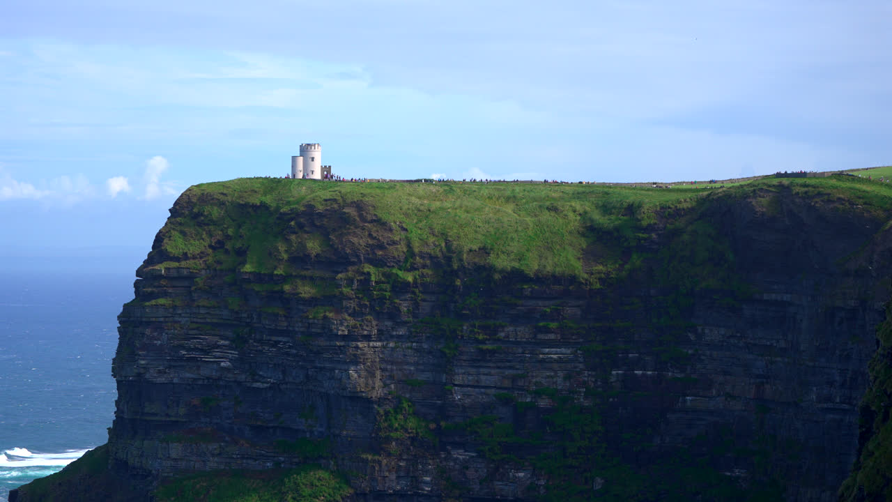 The Cliffs of Moher rise dramatically above the Atlantic, with a lone tower standing in the distance. The rugged landscape and steep cliffs capture the wild beauty of Ireland’s west coast.