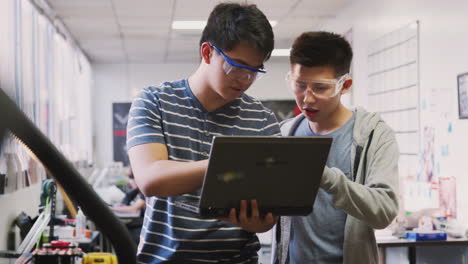 two male college students using laptop computer in science robotics or engineering class