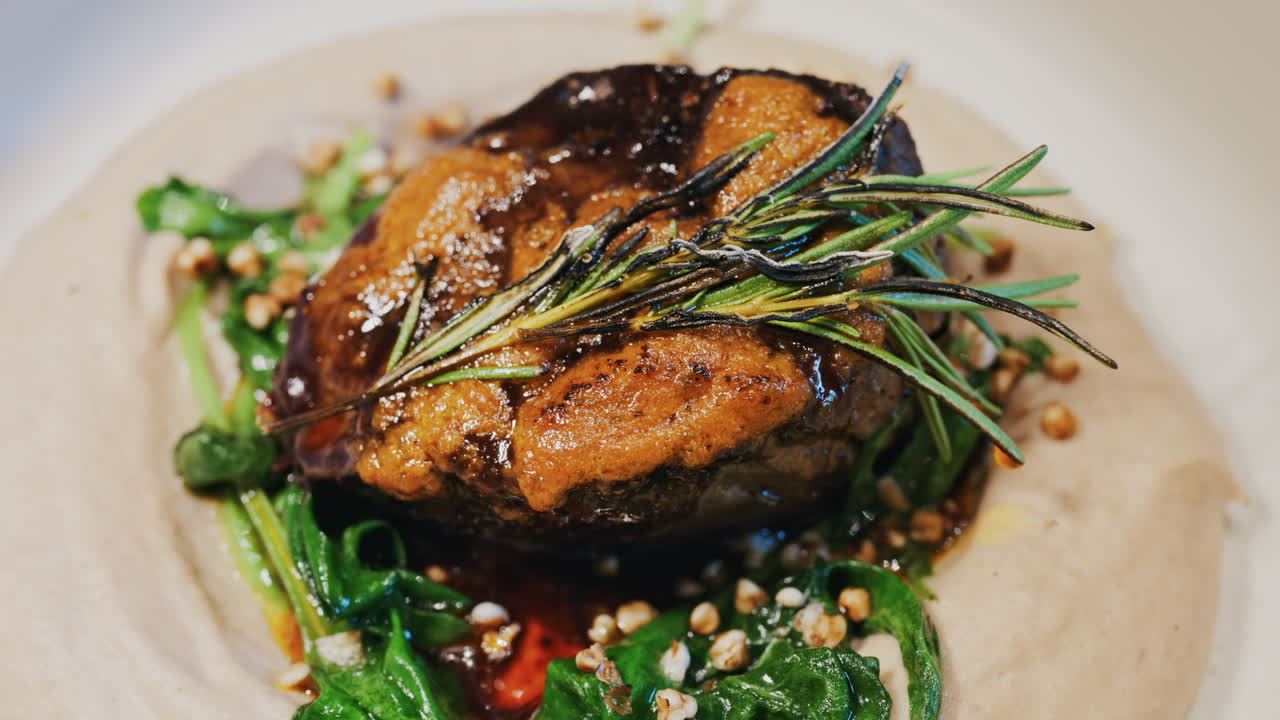 Close up of a beautifully plated beef filet, topped with a golden crust and garnished with rosemary