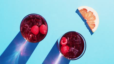 close up of drinks with raspberries and grapefruit over blue background