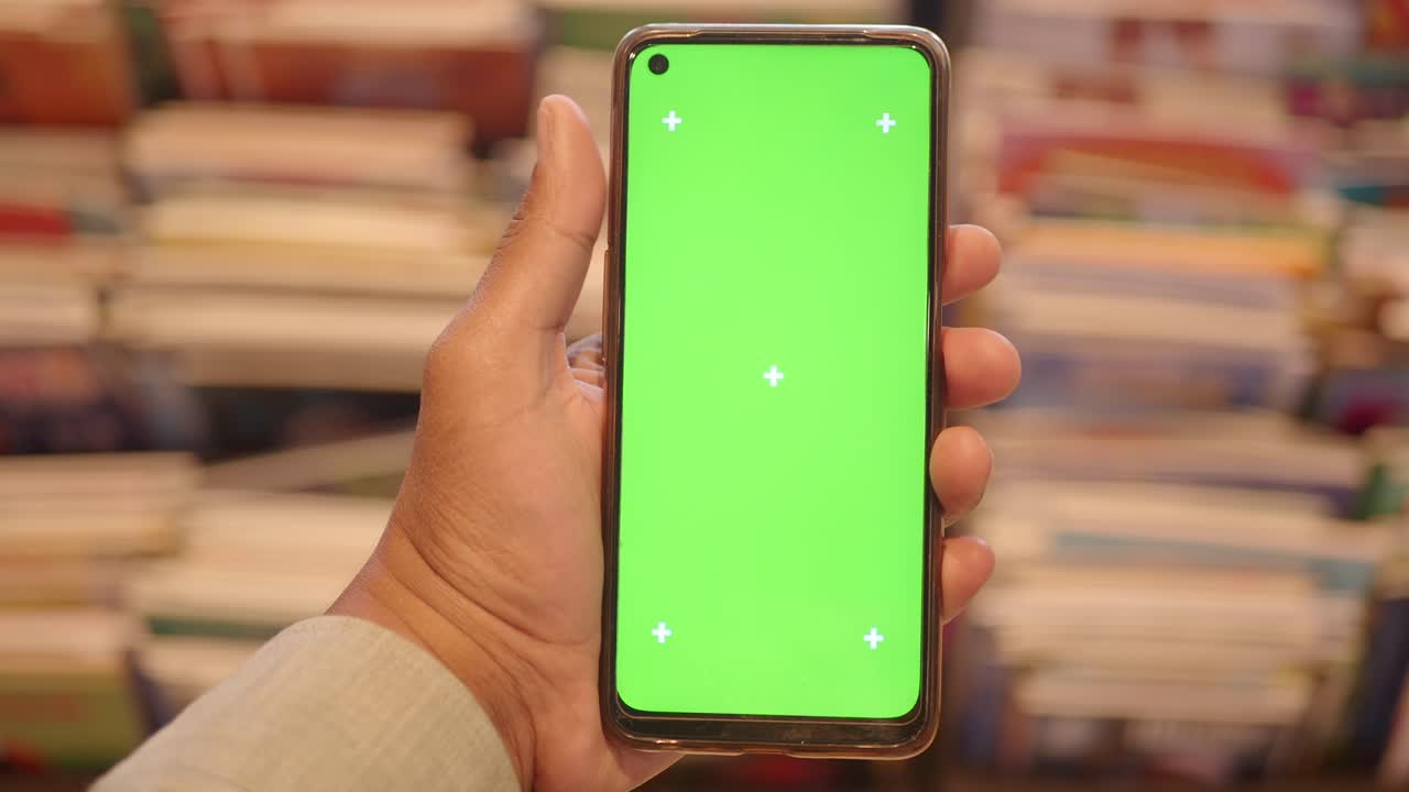 Mano che tiene uno smartphone con schermo verde in una biblioteca