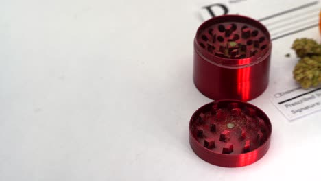 revelación lenta de un molinillo rojo y una botella de prescripción de marihuana abierta con flores derramándose sobre una libreta de recetas en blanco