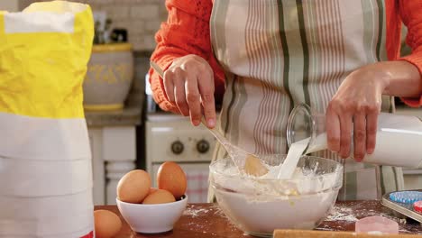 Woman-wearing-apron-pouring-milk-into-the-mixture-in-the-kitchen-4K-4k