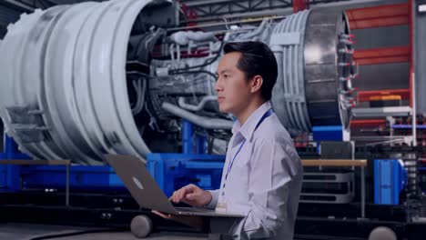 side view of an asian male worker with airplane engine maintenance conducted, analytics checking the turbine, observes by looking up before he come to concentrating on the laptop and keep on typing