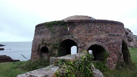 Walking-towards-overgrown-Porth-Wen-abandoned-brickwork-furnace-ruins,-Anglesey-industrial-site