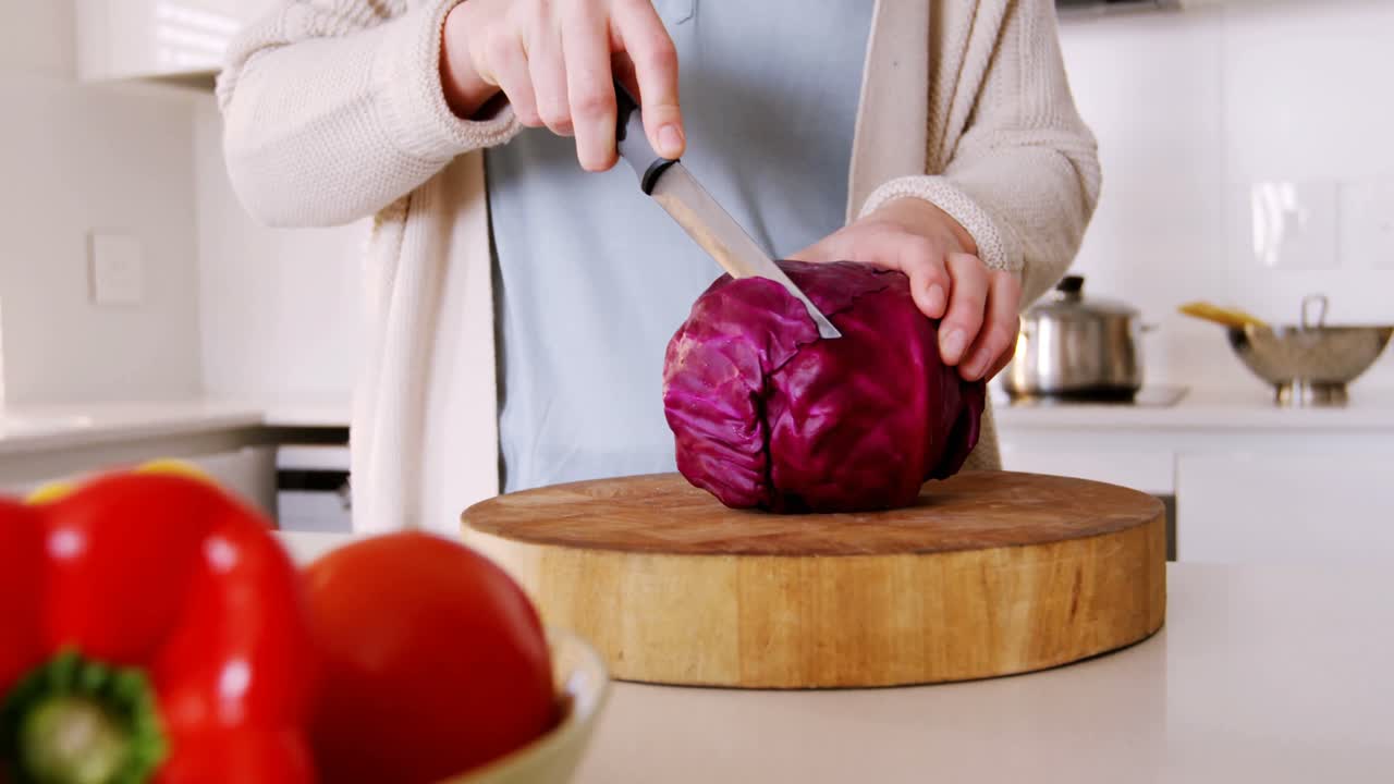 Mid section of woman cutting red cabbage in kitchen