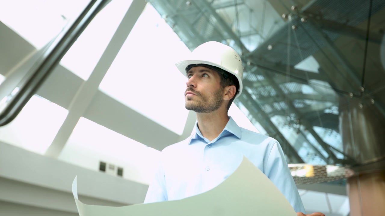 Ingeniero con casco examinando planos en un edificio moderno.