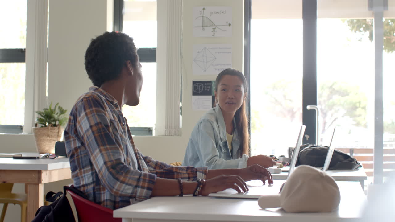 Teenagers in high school using laptops and talking in classroom setting