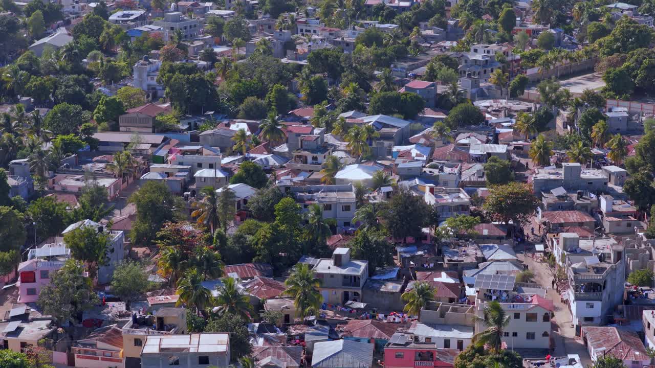 Luftfoto af Juana Méndez i Haiti, der viser tæt bebyggelse, blandede hustage, palmetræer, smalle gader og tæt bystruktur i skarpt dagslys