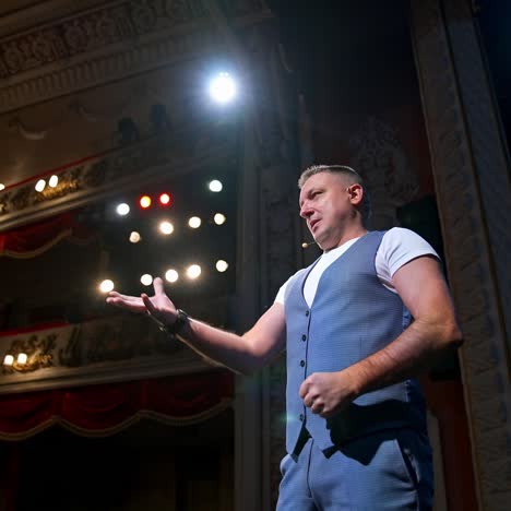 showman entertains the audience under the light, side view. big stage. serious performer speaks from the stage with streched hands