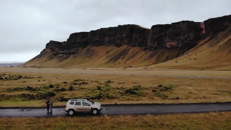 Aerial-view-of-a-Dacia-Duster-SUV-car-parked-on-a-gravel-road-surrounded-by-green-lava-moss-in-Icelandic-countryside-with-a-beautiful-mountain-landscape,-Iceland,-Europe,-Establishing-shot