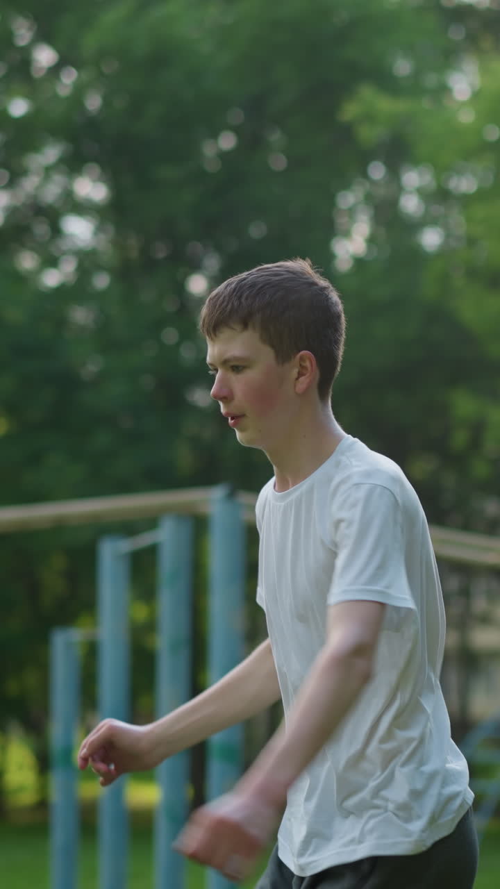 un niño en una camisa blanca, intensamente enfocado en su entrenamiento al aire libre mientras salta, con varios equipos deportivos y árboles en el fondo