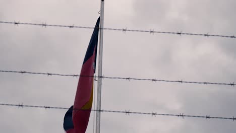 australian aboriginal flag framed by barbed wire on a windy, overcast day