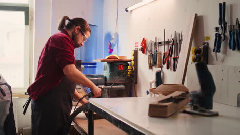 Carpenter-collaborating-with-apprentice,-using-orbital-sander