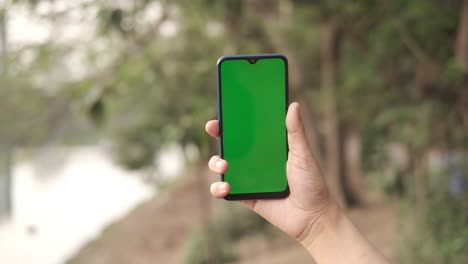 person holding a smartphone with green screen outdoors