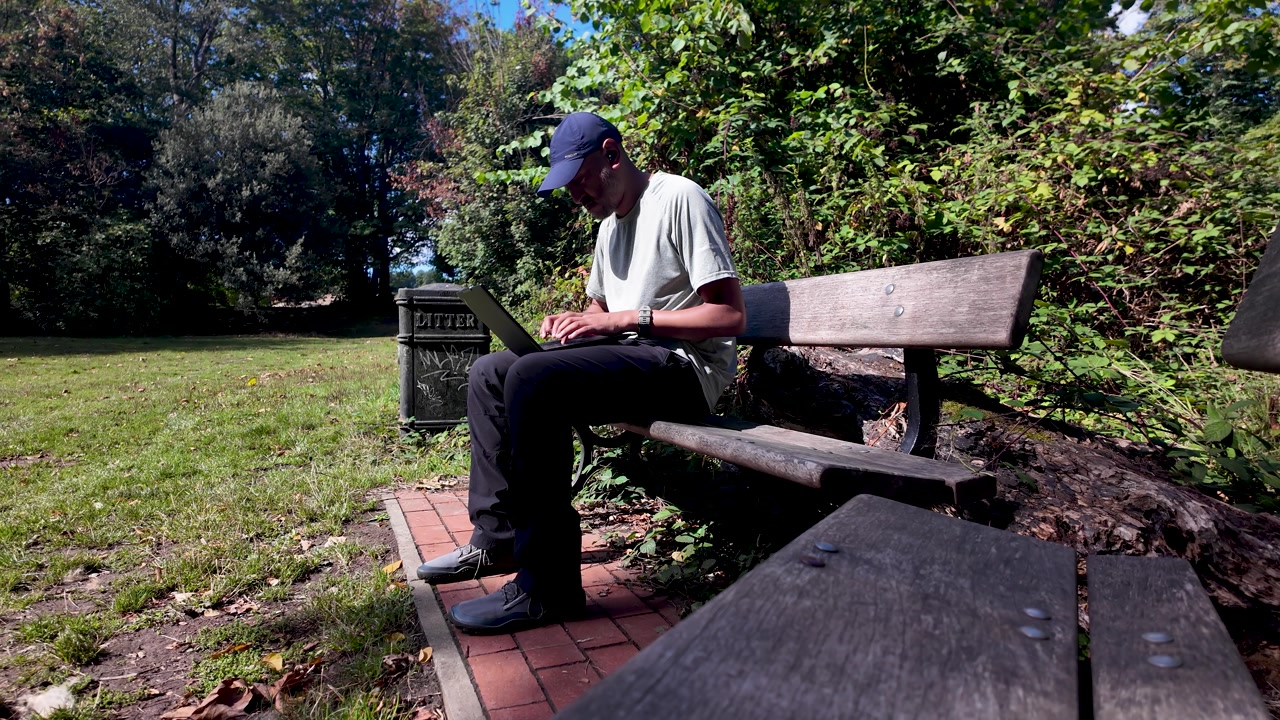 South asian male freelancer working outdoors in park on laptop, enjoying fresh air and sunlight