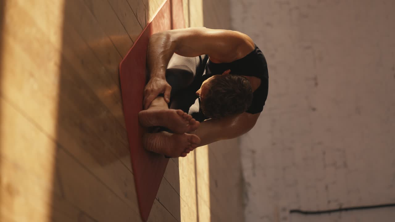 Shooting close up vertical video male athletes in black sports summer uniform doing stretching on the red mat in the Sunny Hall