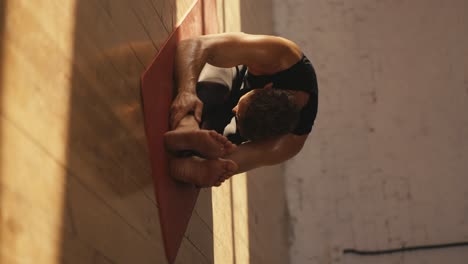 shooting close up vertical video male athletes in black sports summer uniform doing stretching on the red mat in the sunny hall