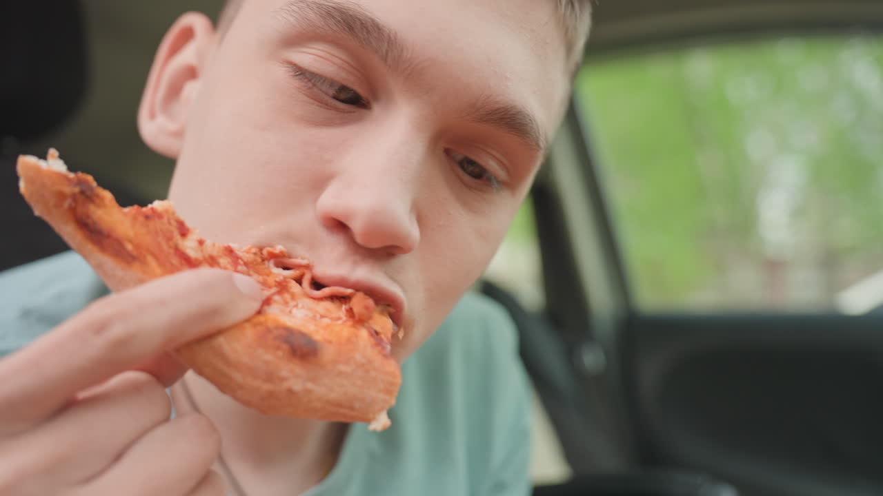 Teen Smiling While Holding Pepperoni Slice In Car, Close Joyful Reaction And Playful Grin Warm Indoor Light, Cheesy Fingertips, Casual Intimacy, Candid Expression Of Satisfaction And Fun During Quick