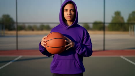 young person in purple hoodie holding basketball on outdoor court