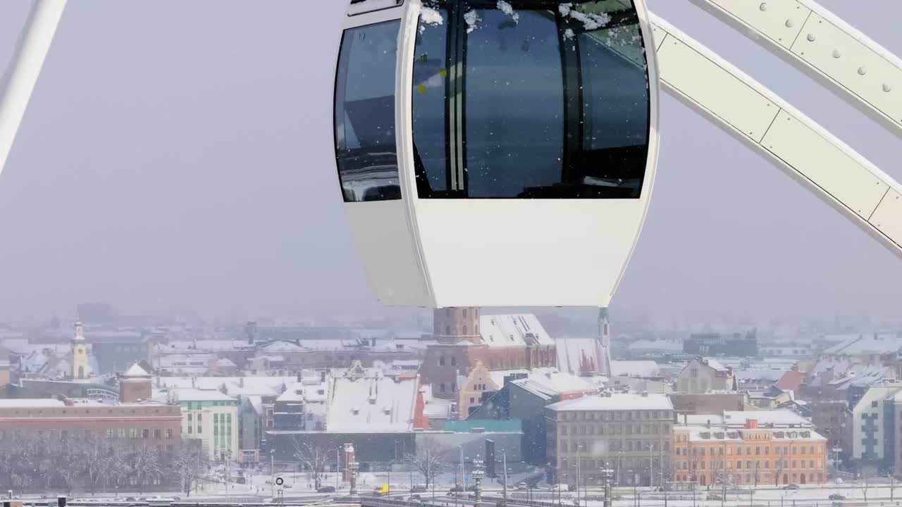 Sideways drone motion reveals snowy Ferris wheel and old Riga in soft sunlight