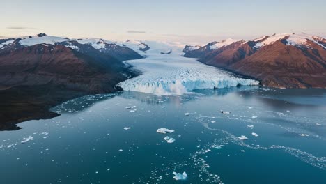 mesmerizing aerial view of a glacial landscape featuring giant icebergs flowing into a serene fjord surrounded by majestic snow-capped mountains at sunset