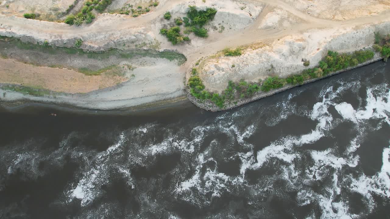 Top-down view of river currents against dry, semi-vegetated terrain with traces of agriculture