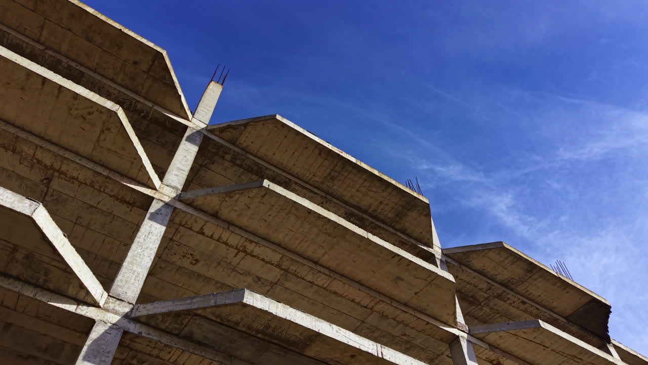 Il cielo azzurro brillante contrasta con la struttura di un edificio incompiuto che si protende verso il cielo, mettendo in mostra l'essenza dello sviluppo urbano sotto la calda luce del sole pomeridiano